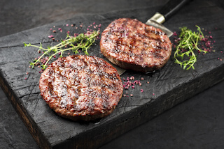 Barbecue Wagyu Hamburger with red wine salt and herbs as closeup on a charred wooden board