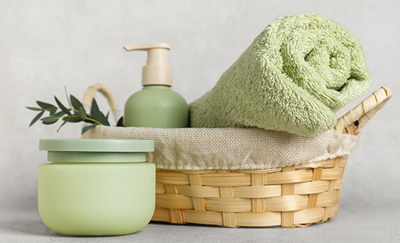 Olive round container next to wicker basket with light olive towel and soap dispenser