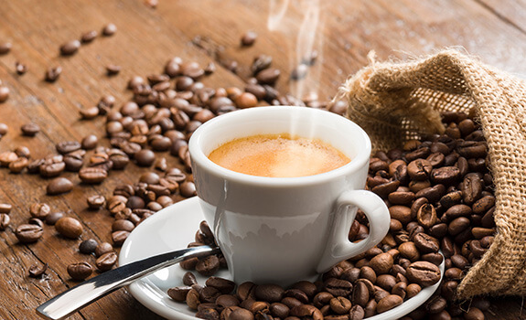 Small white cup of shroom caffe, on top of a coffee beans
